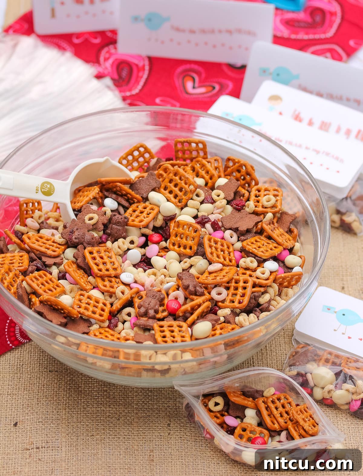 homemade trail mix in a mixing bowl for Valentine's day with gift bags and tags next to it.