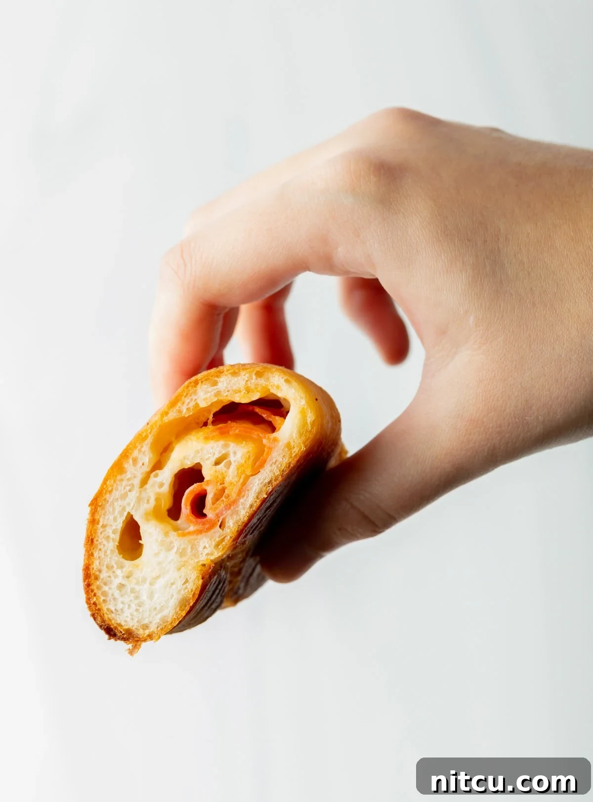 hand holding half of a pizza roll with cheese and meat