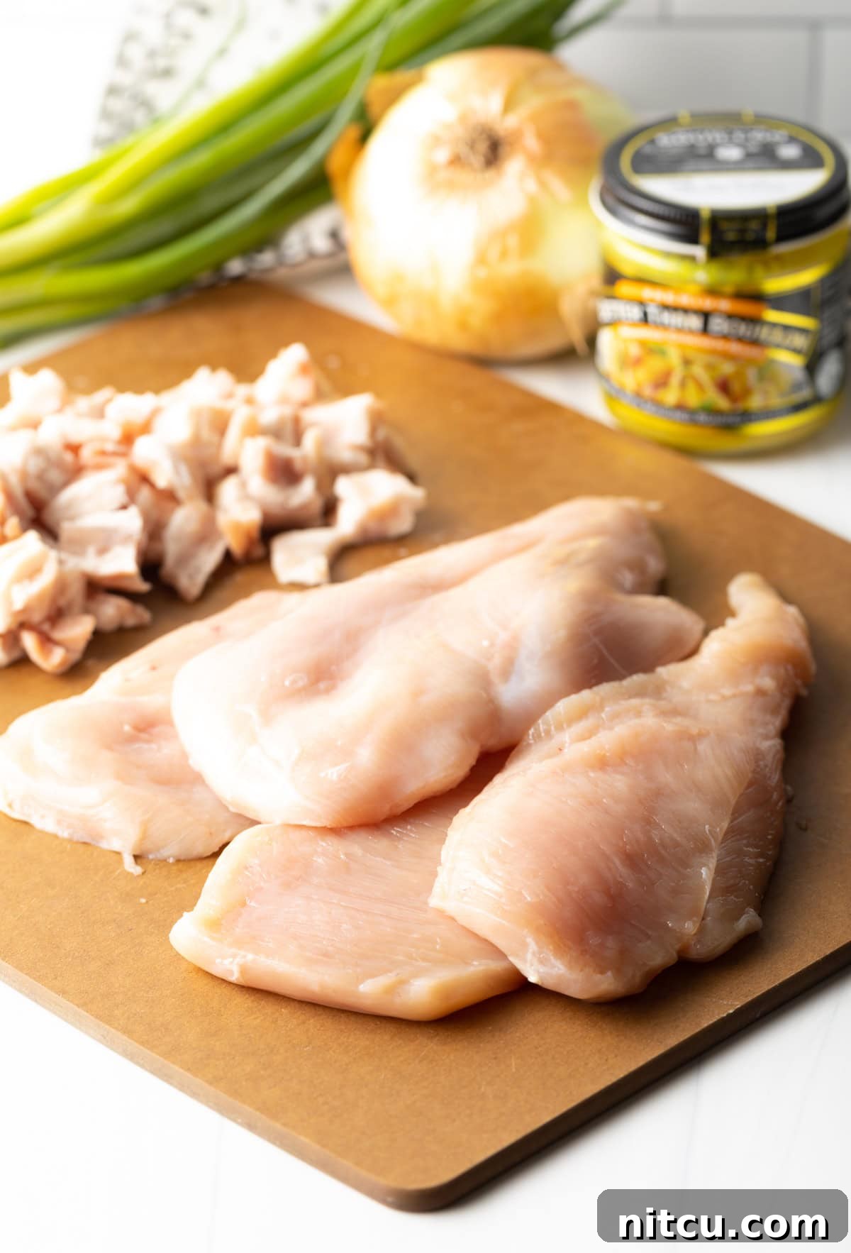Ingredients for Smothered Chicken laid out on a cutting board, including raw chicken breasts, bacon, onion, and spices.