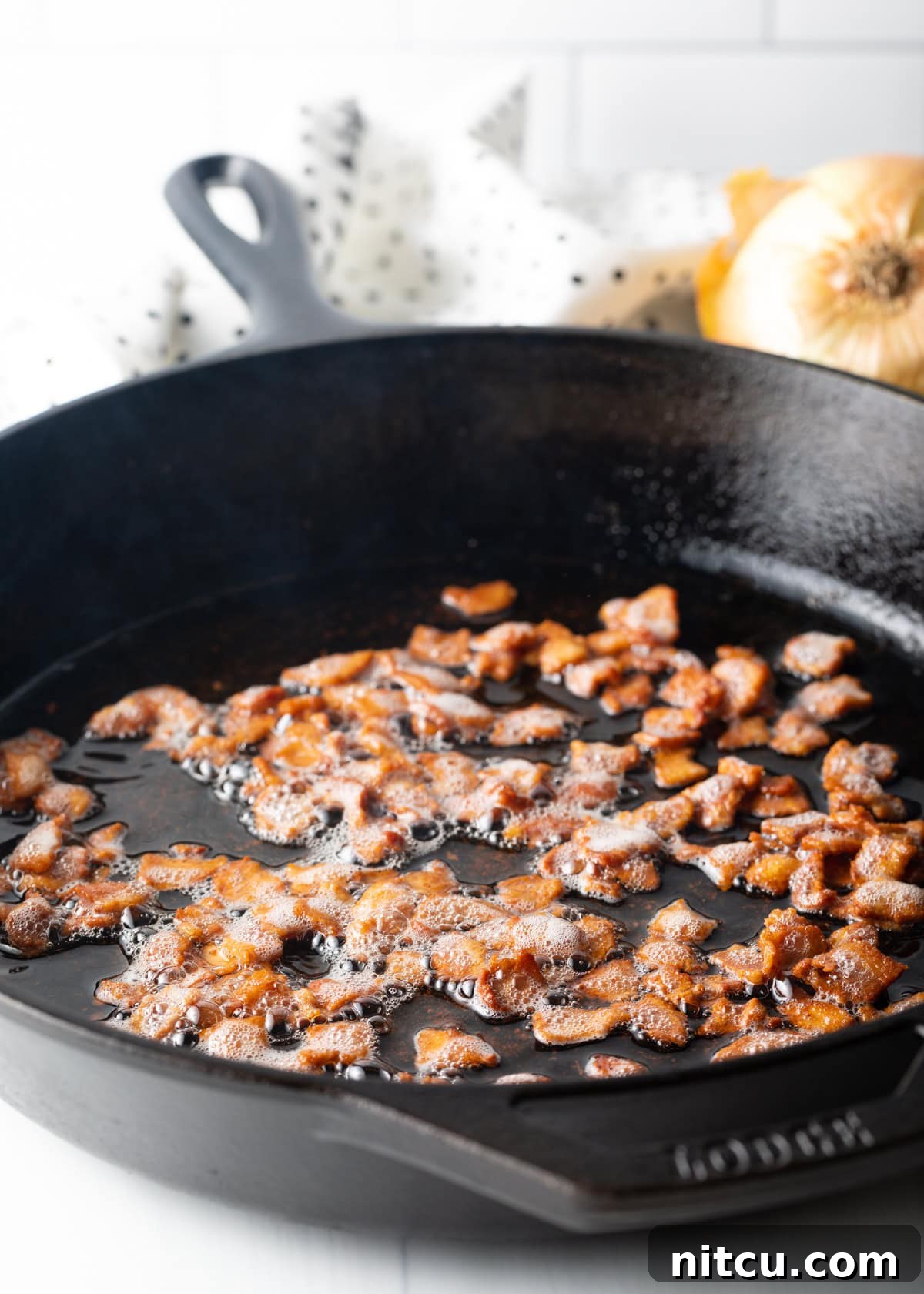 Close-up of chopped bacon sizzling and browning in a cast iron skillet.