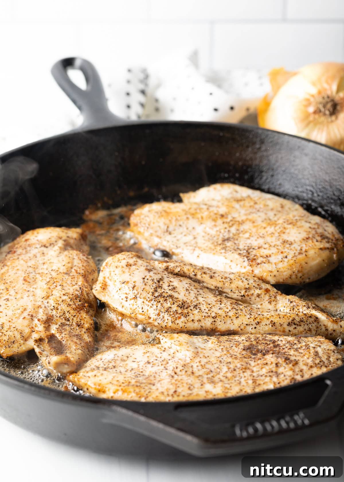Seasoned chicken breasts cooking to a golden brown in a cast iron skillet with hot bacon grease.