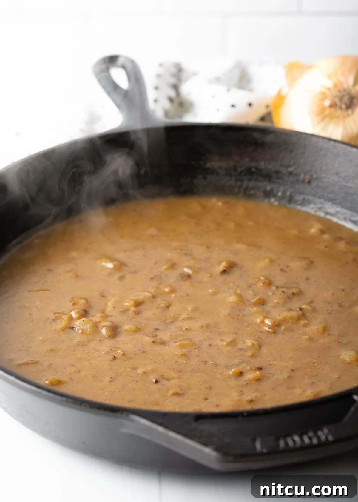 Rich, brown gravy simmering and thickening in a cast iron skillet on the stovetop.