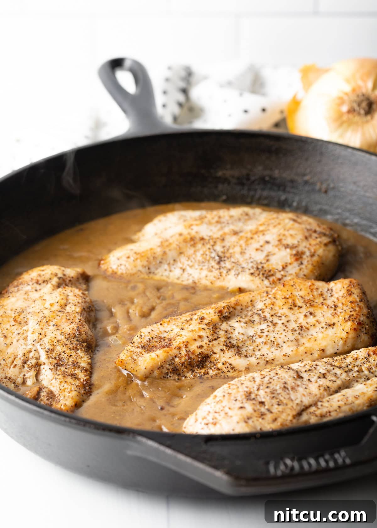 Tender chicken breasts coated in a rich brown gravy, simmering in a heavy cast iron skillet.