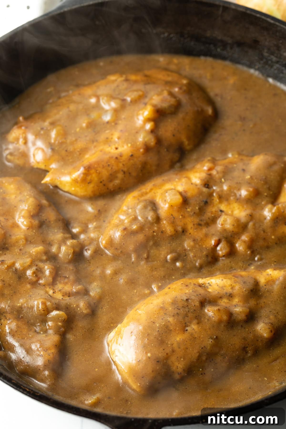 Overhead view of boneless, skinless chicken smothered in rich gravy with melted cheese, bacon, and scallions in a cast iron skillet.