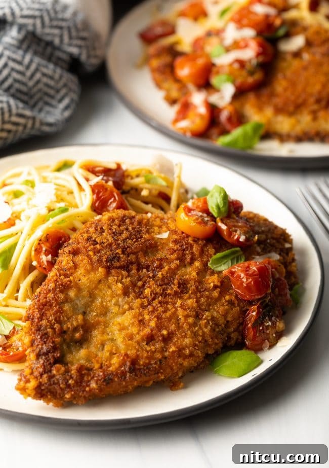 side view breaded fried Italian chicken cutlets on a plate with pasta and tomatoes and micro basil