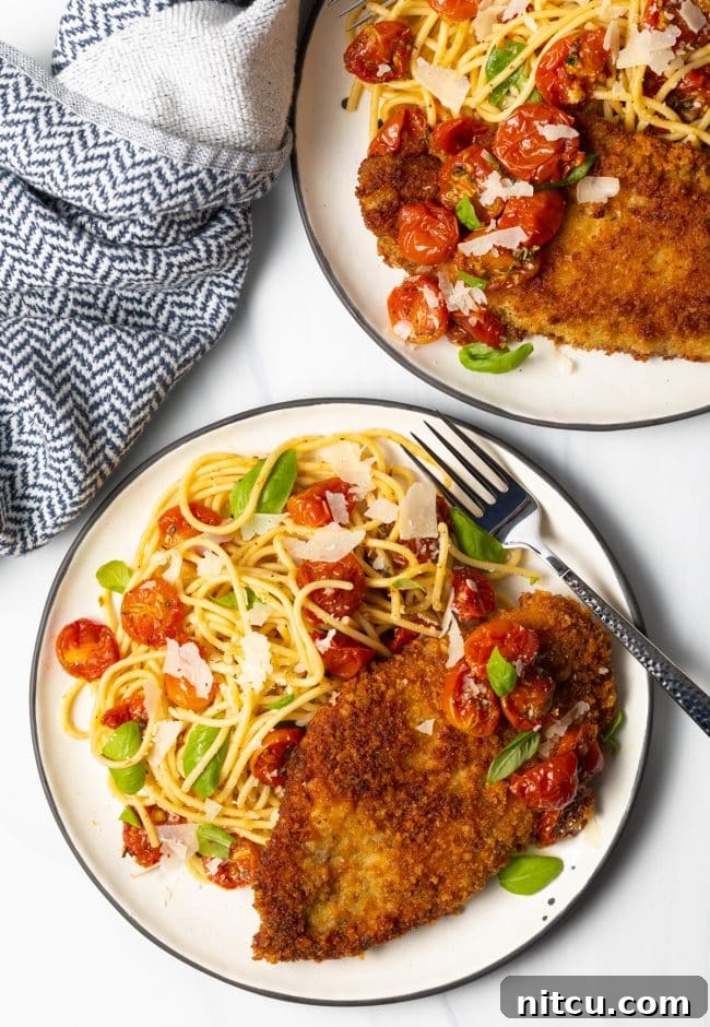 overhead view two plates of pasta with fried chicken breasts and cherry tomato sauce