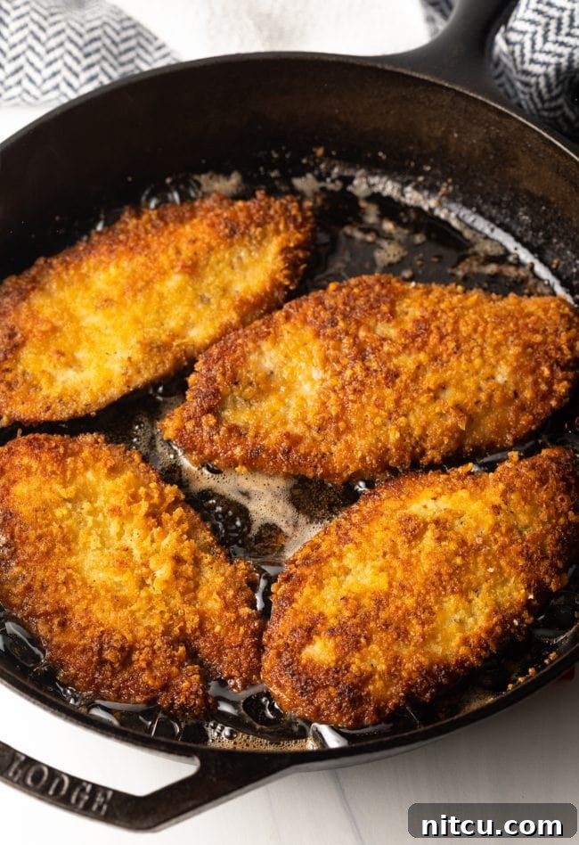 large cast iron pan frying crispy chicken cutlets with Italian marinade and seasoning