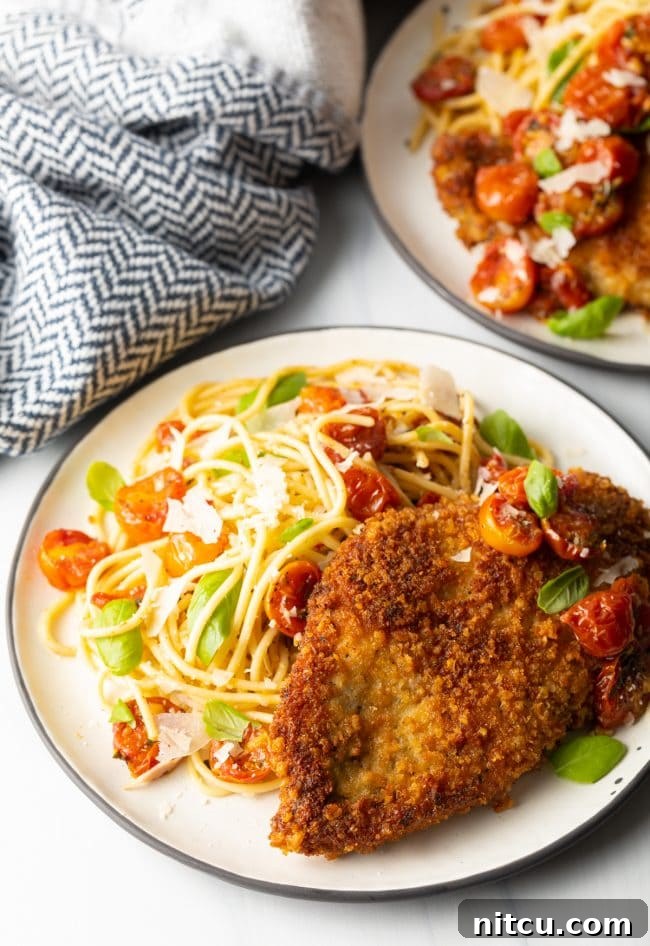 finished plate of pan fried or oven baked crispy Italian chicken cutlets with pasta and cherry tomato sauce on the side