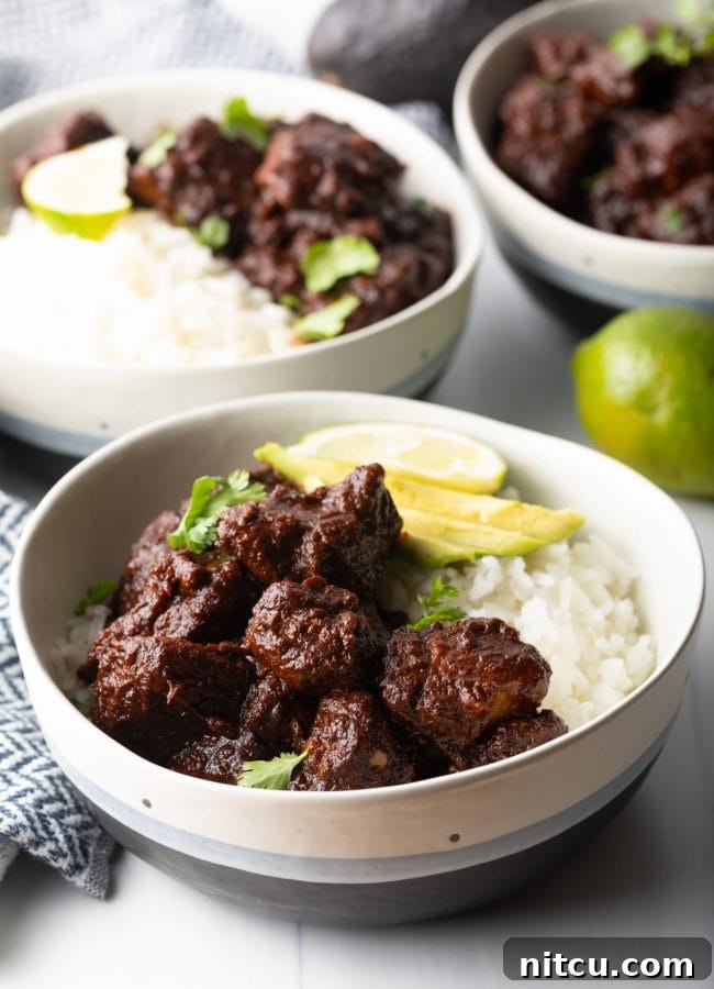 side view red chile pork carne adovada in a bowl with white rice, avocado, lime and cilantro