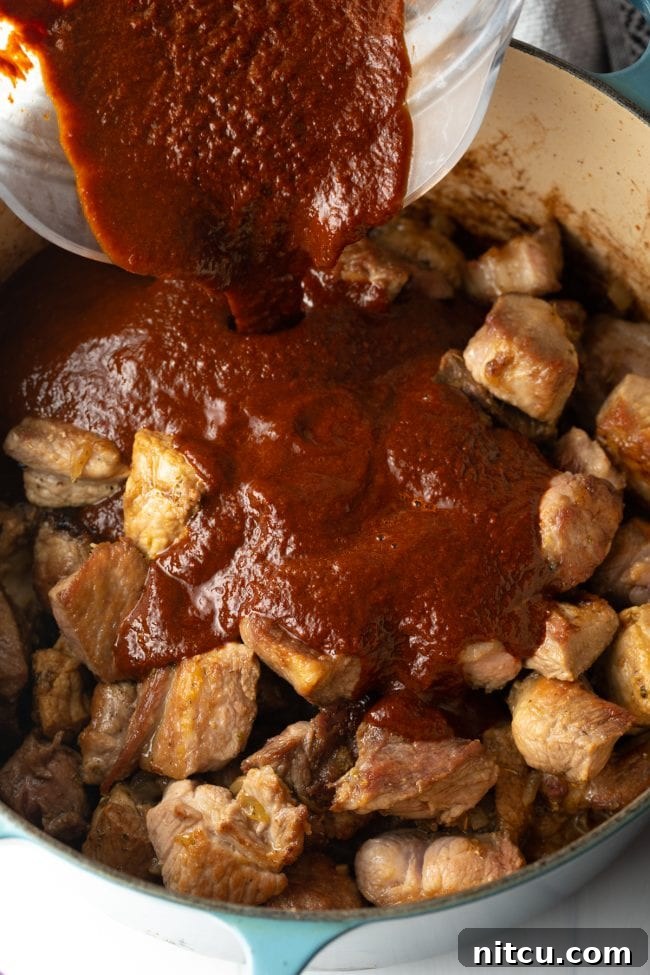 adding the smoky sauce to the chunks of seared pork in the pot