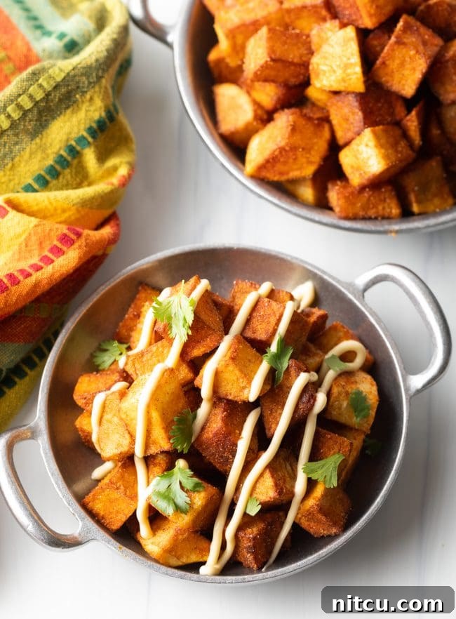 Overhead view of two bowls of Mexican fried potatoes with creamy aioli and chopped cilantro garnish
