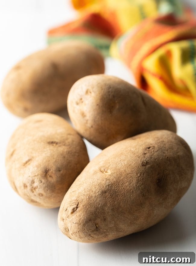 Whole russet potatoes on a clean white background, ready for preparation