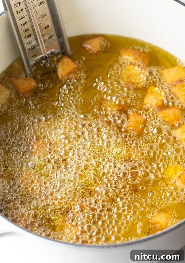 Potatoes frying in hot oil in a large pot, with a thermometer clipped to the side