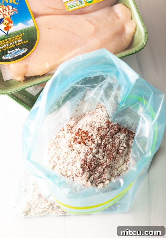 A clear plastic zipper bag brimming with a seasoned flour mixture, poised beside a package of raw, boneless chicken breasts – the essential components for our French chicken recipe.