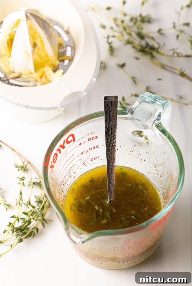A clear glass measuring cup holds a vibrant mixture of olive oil, fresh lemon juice, minced garlic, and assorted seasonings, poised to create the savory pan sauce.