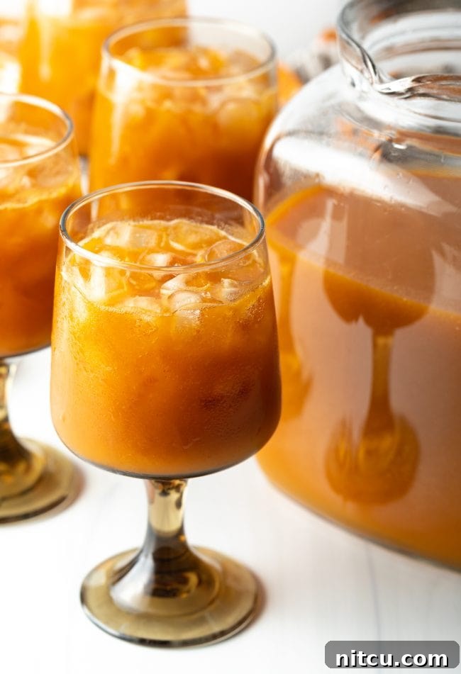glass of iced juice with pumpkin puree and fruit over ice, next to a pitcher of juice