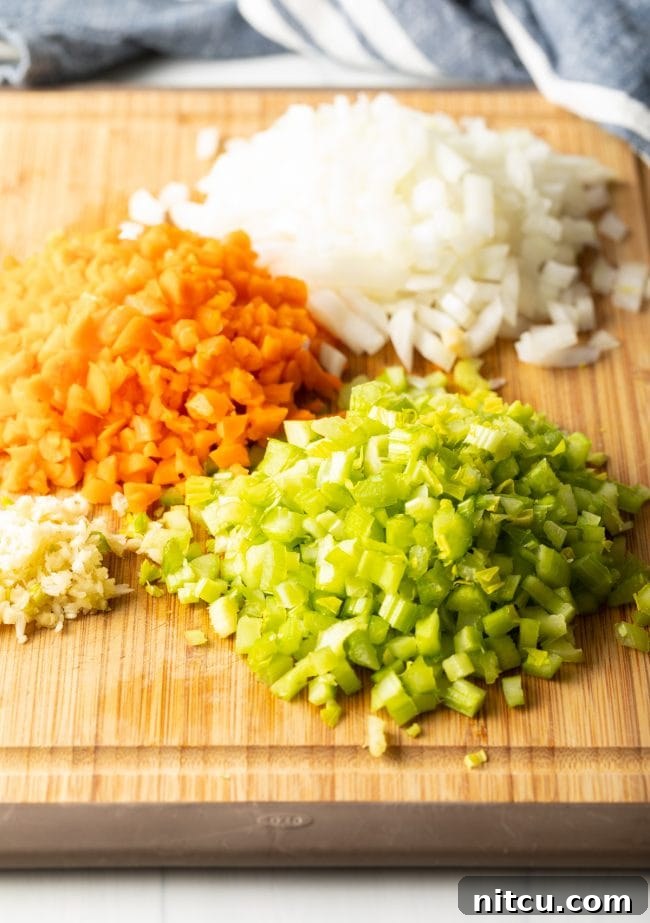 A wooden cutting board displaying neatly piled chopped celery, carrots, onion, and minced garlic, ready for making the easy rigatoni bolognese sauce.