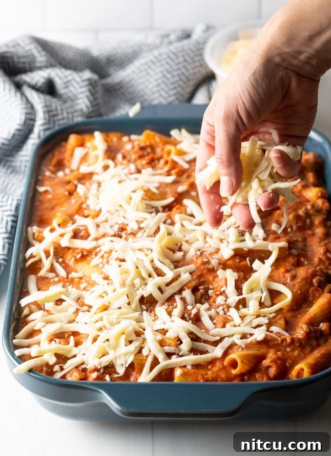 Adding a generous sprinkle of shredded mozzarella cheese over the top of the rigatoni pasta casserole in the baking dish, ready for the oven.