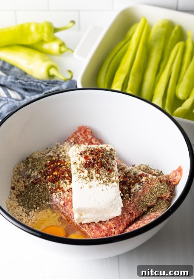 Various ingredients for the sausage stuffing, including ground sausage, cream cheese, and spices, arranged in a bowl before mixing