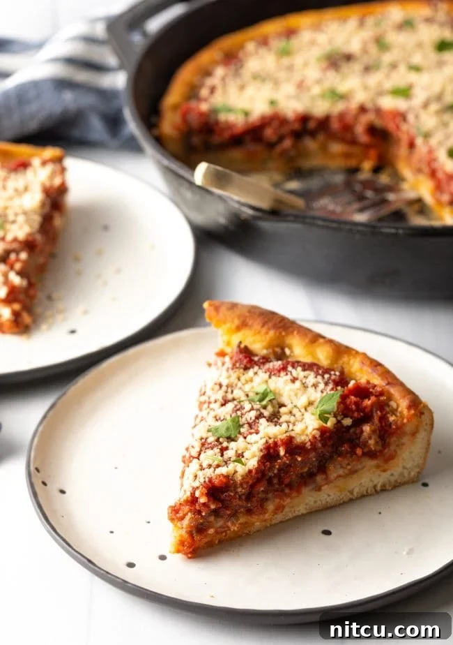 A delectable slice of deep dish pizza on a plate, with the cast iron skillet visible in the background, showcasing its thick, golden crust and rich layers of cheese and sauce.