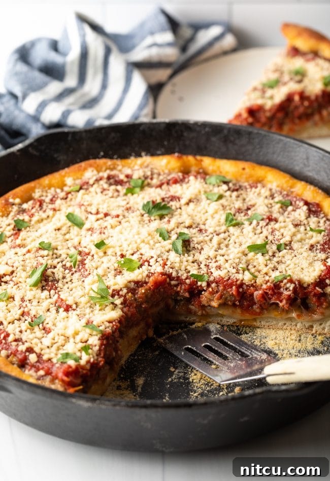 A tempting side view of a freshly baked cast iron deep dish pizza, with a single slice removed revealing the generous layers of melted cheese, savory sausage, and robust tomato sauce within its thick, golden crust.