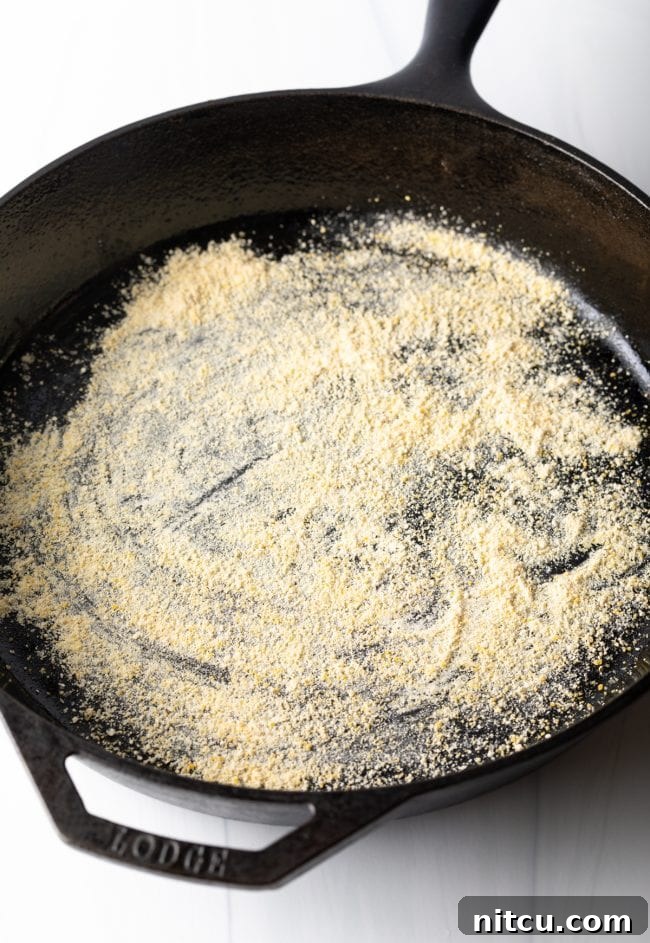 A cast iron skillet generously dusted with golden cornmeal, prepared and ready to receive the pizza dough for a homemade deep dish pizza.