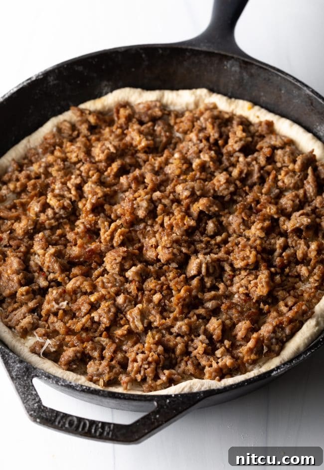 Perfectly browned Italian sausage crumbles layered over the melted cheese and pizza dough, creating a hearty filling for the deep dish pizza.