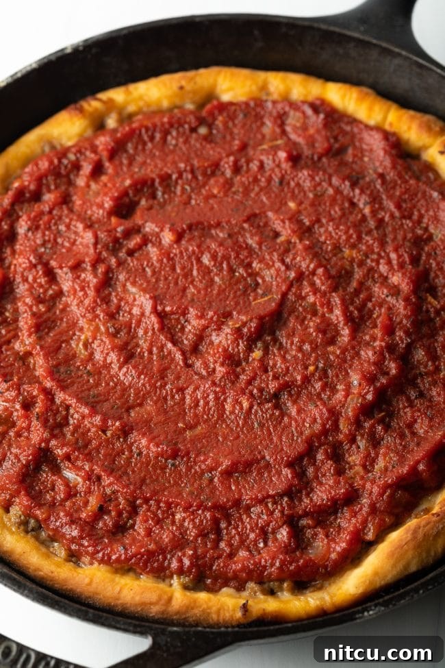A glorious top-down view of the freshly baked deep dish pizza, showcasing its rich red tomato sauce and perfectly golden crust edges, straight from the oven.