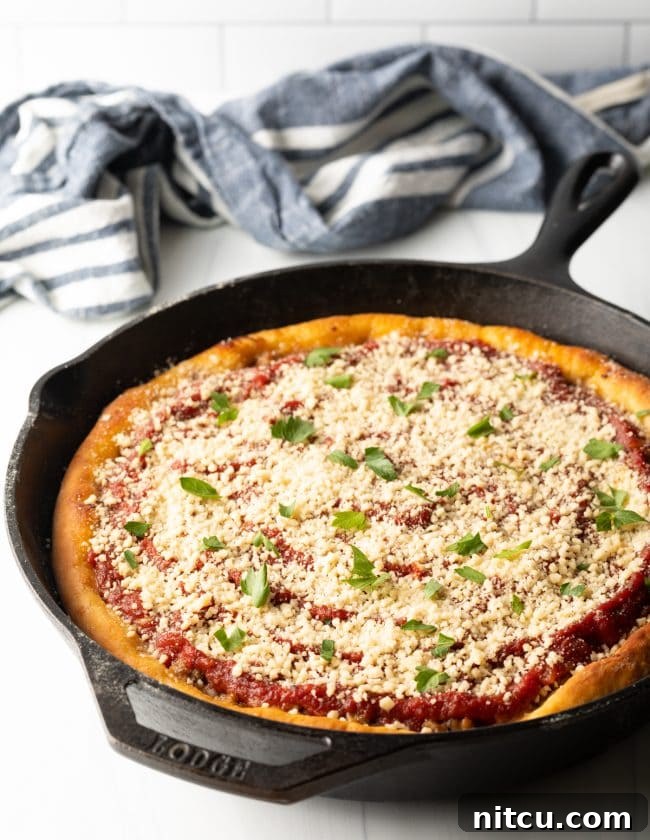 A stunning side-top view of a baked Chicago-style deep dish pizza still nestled in its cast iron skillet, highlighting its impressive height and golden, crispy crust.
