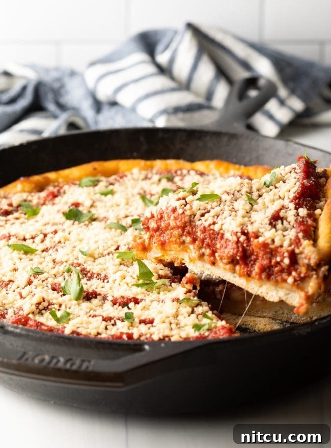 A close-up shot of a perfect slice of deep dish pizza being carefully removed from a hot cast iron skillet, showcasing its thick crust and abundant, melted fillings.