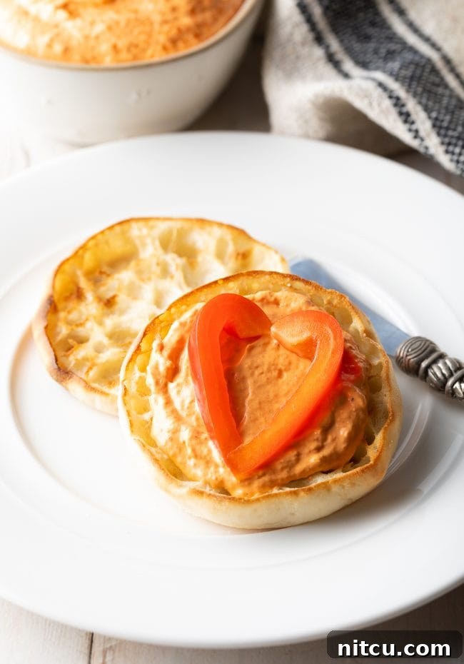 Roasted Red Pepper Dip served on an English muffin with sliced red pepper on top. 
