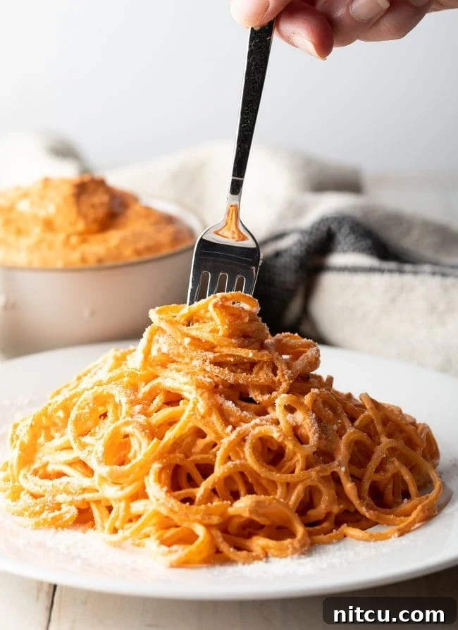 Fork swirling around some noodles coated in roasted red pepper sauce. 