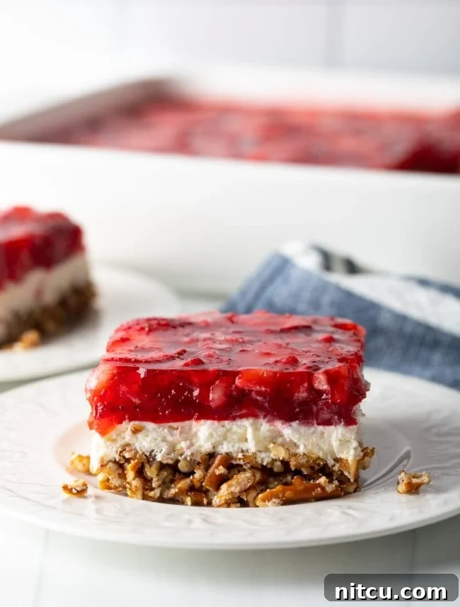 Close-up slice of layered strawberry pretzel salad on a white plate, showcasing the distinct pretzel, cream cheese, and jello layers.
