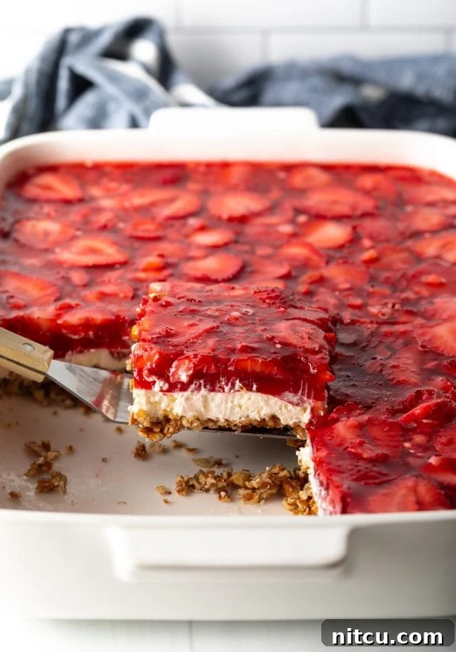 A spatula lifting a perfect piece of strawberry pretzel salad dessert from the baking pan, showing the distinct layers.