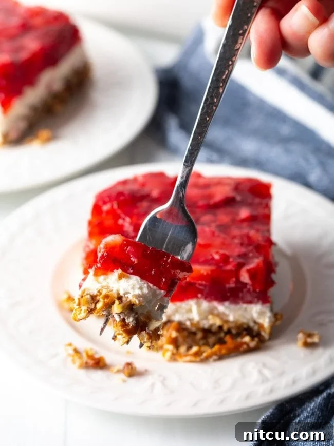 A fork holding a bite of strawberry pretzel dessert salad, showing the distinct layers close to the camera.