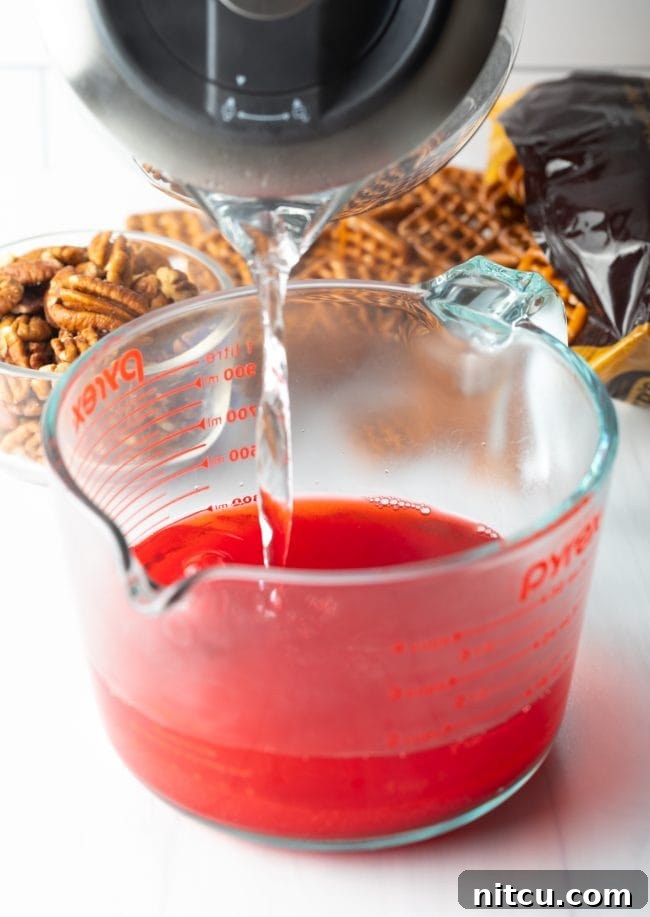 A hand pouring hot water into a bowl containing strawberry gelatin mix.