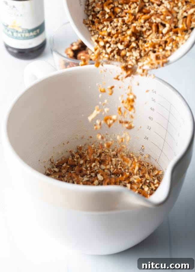 Crushed pretzels being added to a large measuring cup, showing their texture.