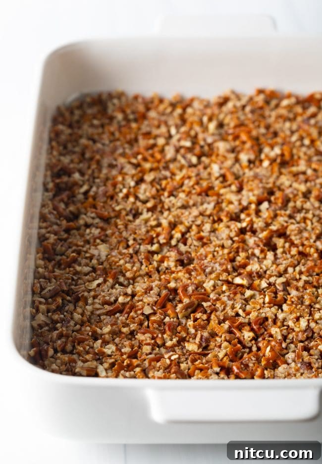 A tightly packed layer of pretzels and pecans forming the crust in the bottom of a white baking dish.