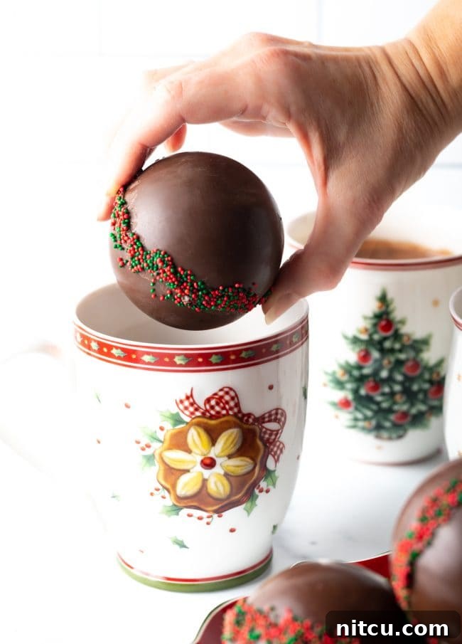 Hand holding hot chocolate ball over a Christmas mug.