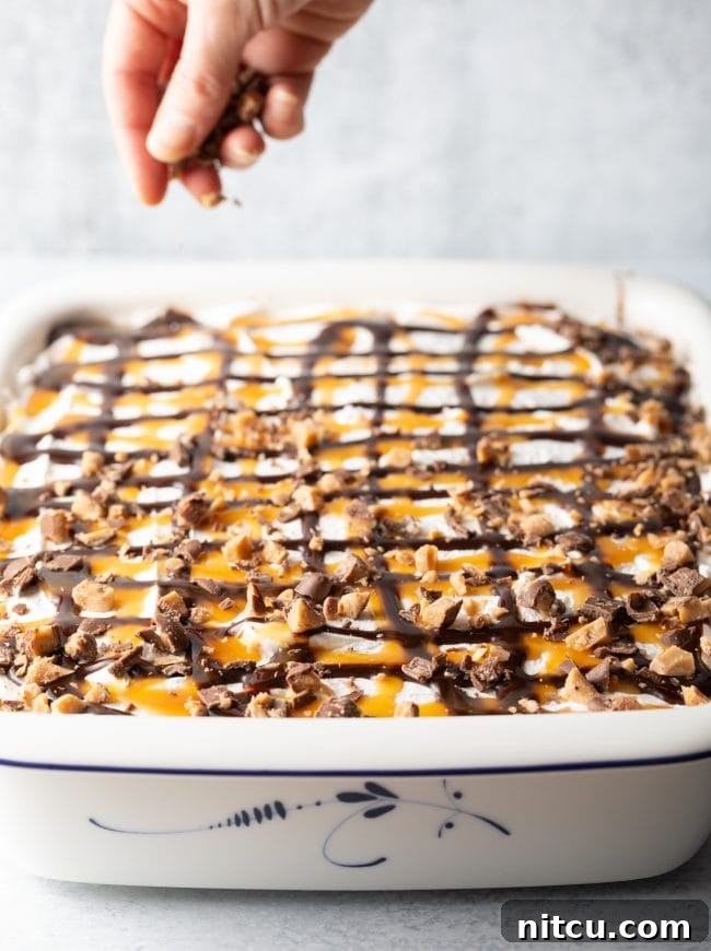 A finished Better Than Sex Cake is shown with chopped Heath bars generously sprinkled on top of the creamy whipped cream, decadent chocolate sauce, and glistening caramel, highlighting its rich and irresistible layers.