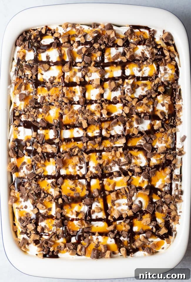 Top-down view of the completed Better Than Sex Chocolate Poke Cake presented in a large white baking dish, elegantly garnished with swirls of chocolate and caramel sauce and a scattering of chopped toffee candy bars, ready to be served.