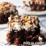 Close-up view of a chocolate poke cake with whipped topping, caramel and chocolate sauce, and chopped Heath bars