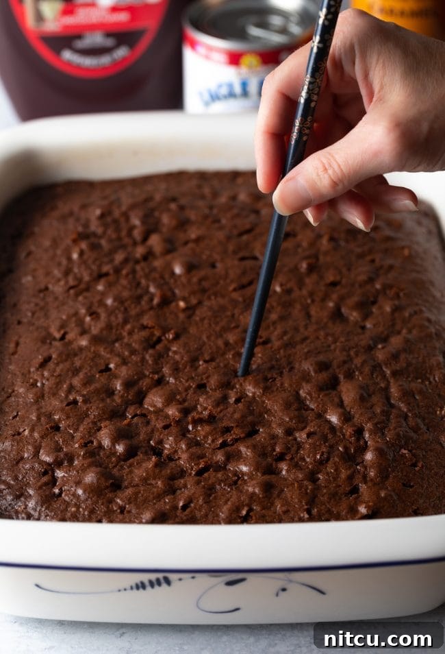A close-up shot shows a chopstick being used to carefully poke holes into the freshly baked Devil's food cake, preparing it for the decadent caramel soak.