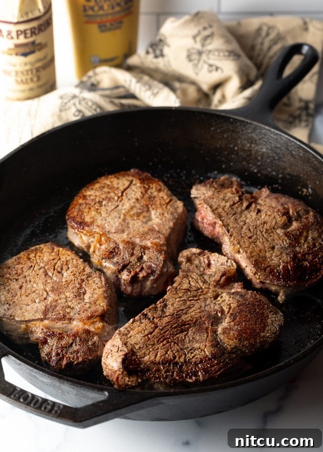 Four perfectly seared steaks resting in a robust cast iron skillet, ready for the luxurious sauce.