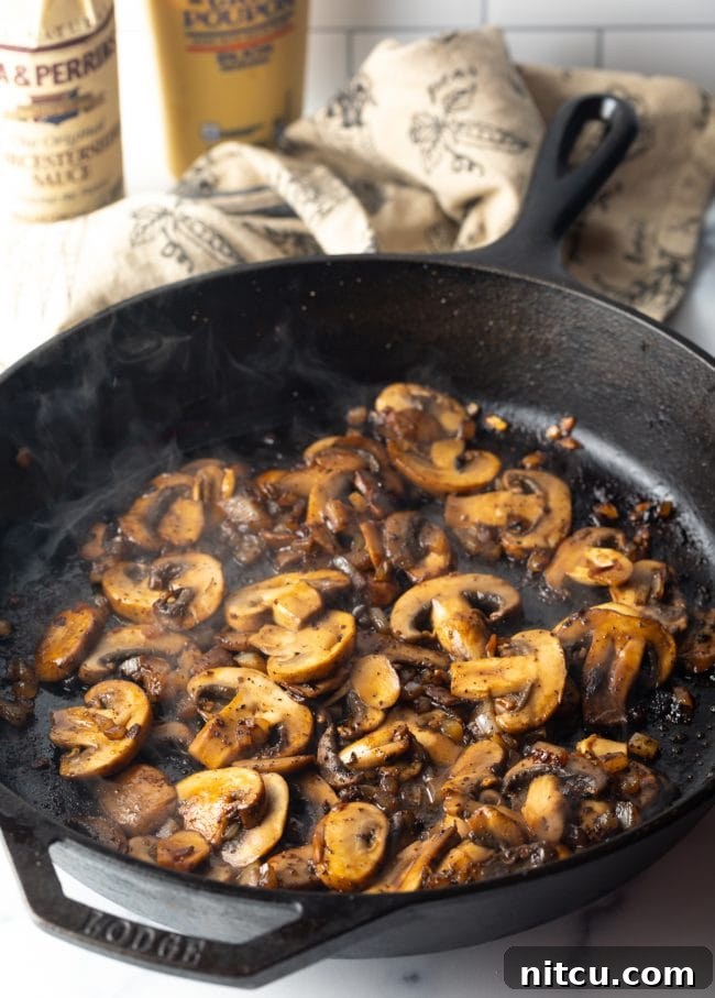 Thinly sliced mushrooms being sautéed in a cast iron skillet, softening and releasing their aroma.