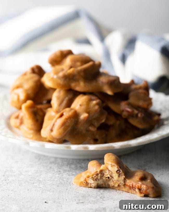 Side view of cinnamon pralines with whole pecans on a white plate, with one candy bitten in half next to the plate to show the interior.