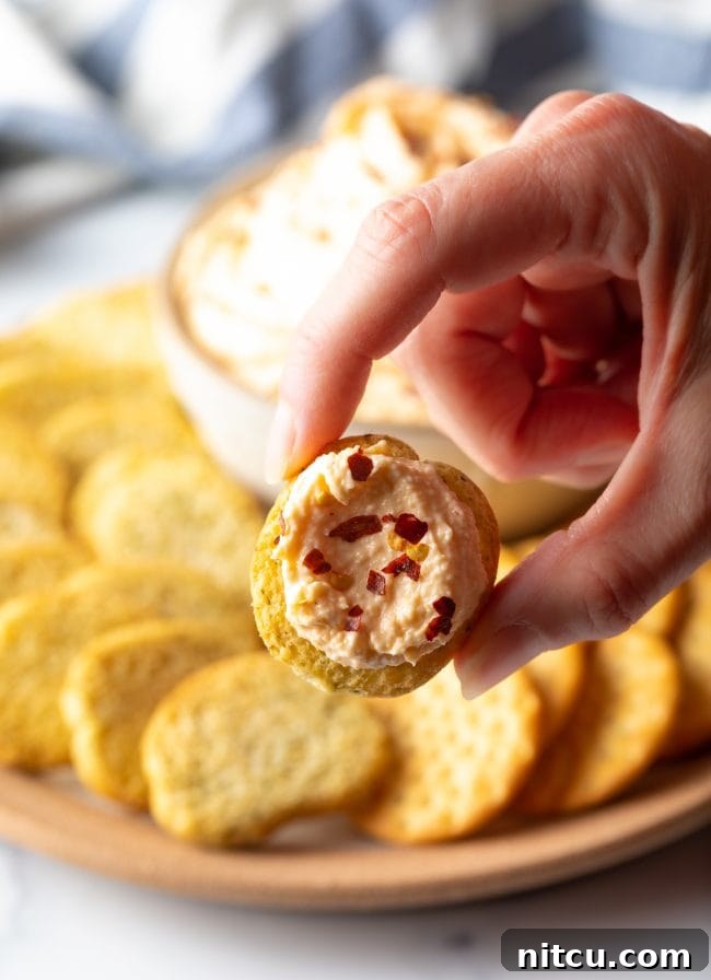 hand holding cracker with smoked gouda spread up to camera