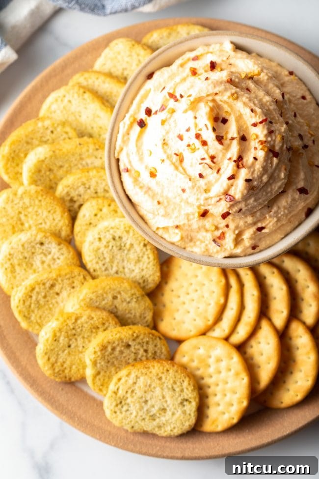 Top view bowl of cheese spread with crushed red pepper on top, surrounded by slices of crunchy bread and crackers.