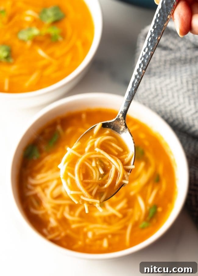 top view of a spoon lifting a bite of Mexican Sopa de Fideo, highlighting the noodles and broth