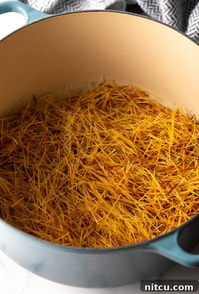 broken fideo pasta browning in a large pot, showing the crucial toasting step